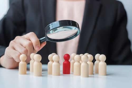 Businesswoman hand holding magnifying glass for recruiting leader man wooden from crowd of employees.Human resource management, Recruitment, Teamwork, hiring and leadership Concepts